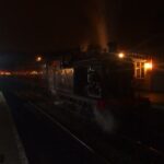 A steam train glowing with warm lights at a station at night
