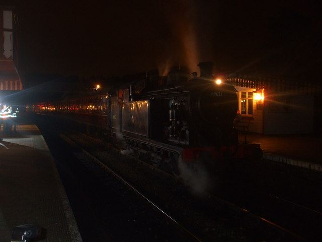 A steam train glowing with warm lights at a station at night